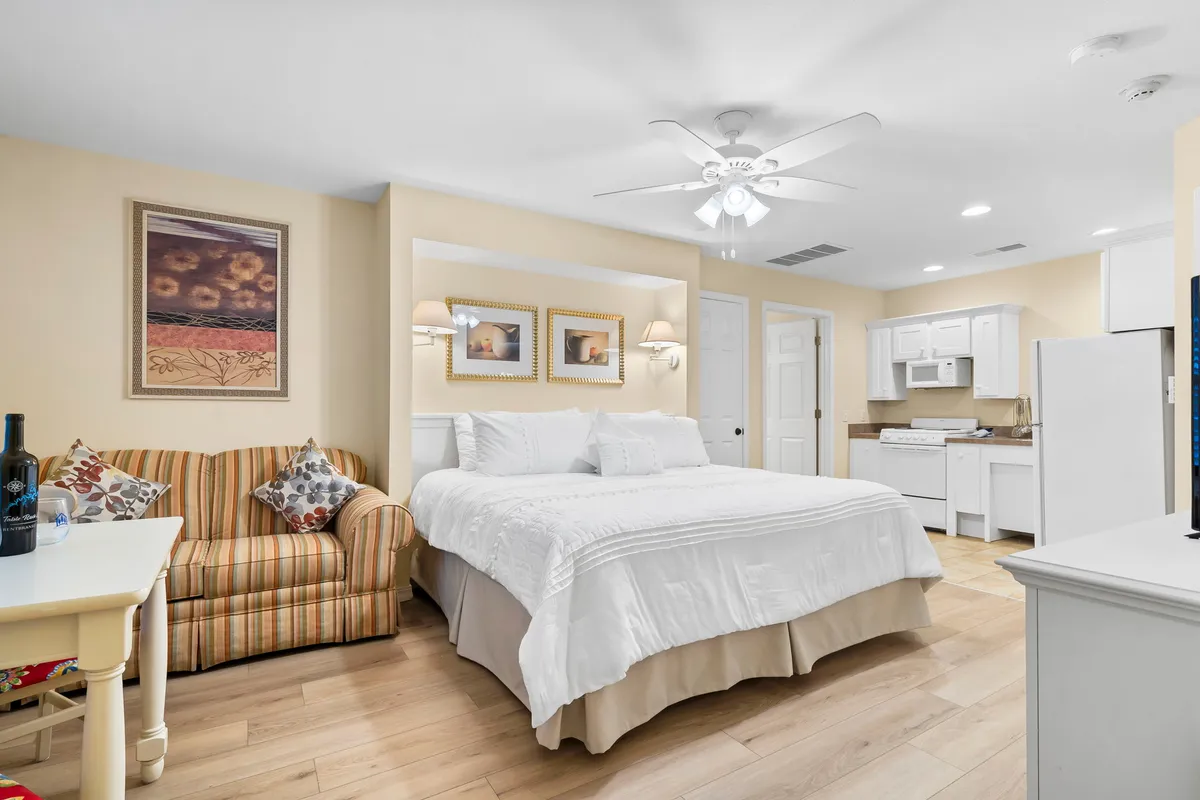 A cozy suite that includes a large bed, a striped sofa for lounging, a small dining table for in-room meals or morning coffee, and a convenient kitchenette. The setting feels warm and homey, ideal for couples, parents, or grandparents seeking their own inviting space.