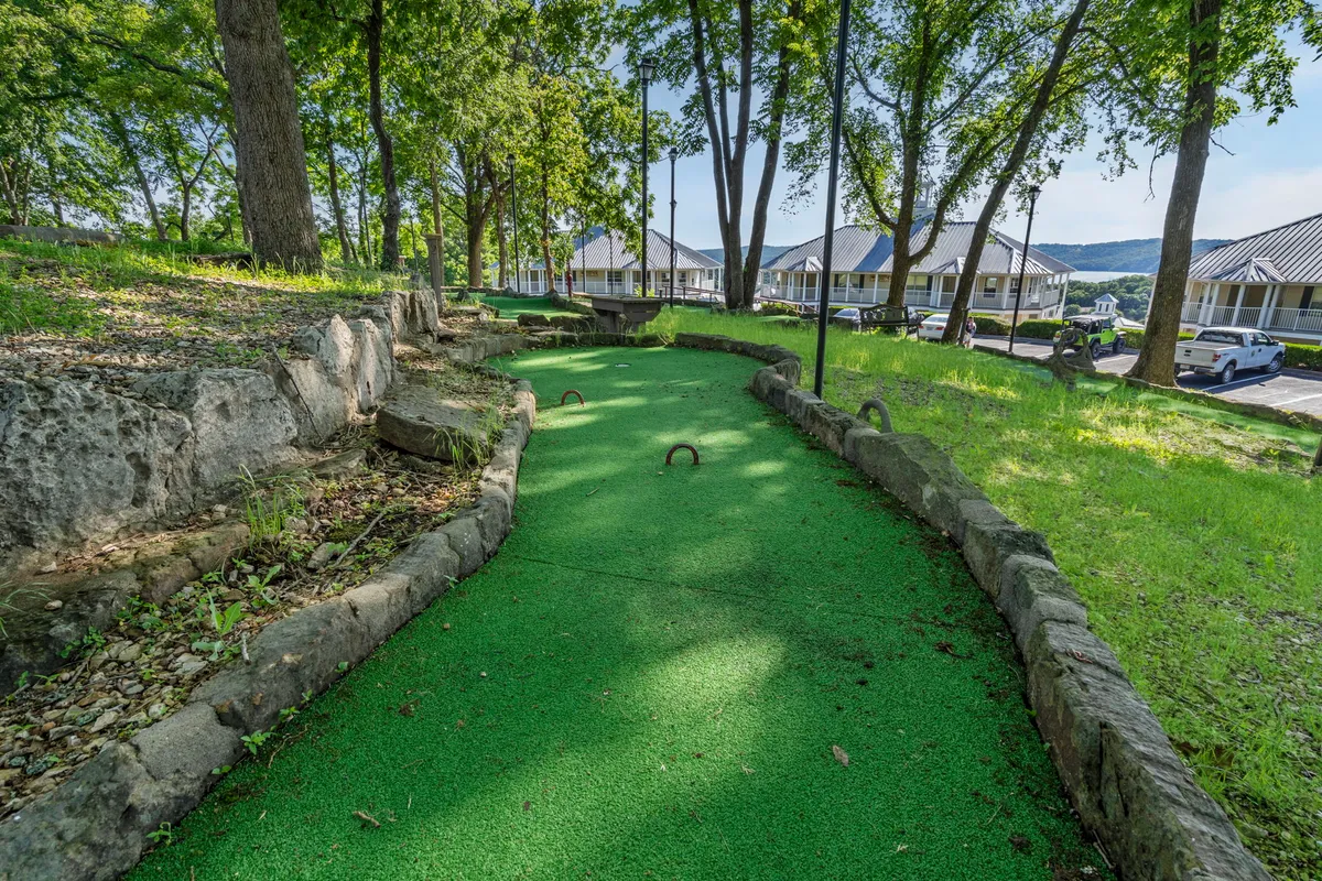 A vibrant mini-golf course with lush green synthetic turf winds through a natural landscape, inviting families to engage in friendly competitions. Trees and gentle landscaping provide a playful, shaded environment perfect for laughter and memory-making.