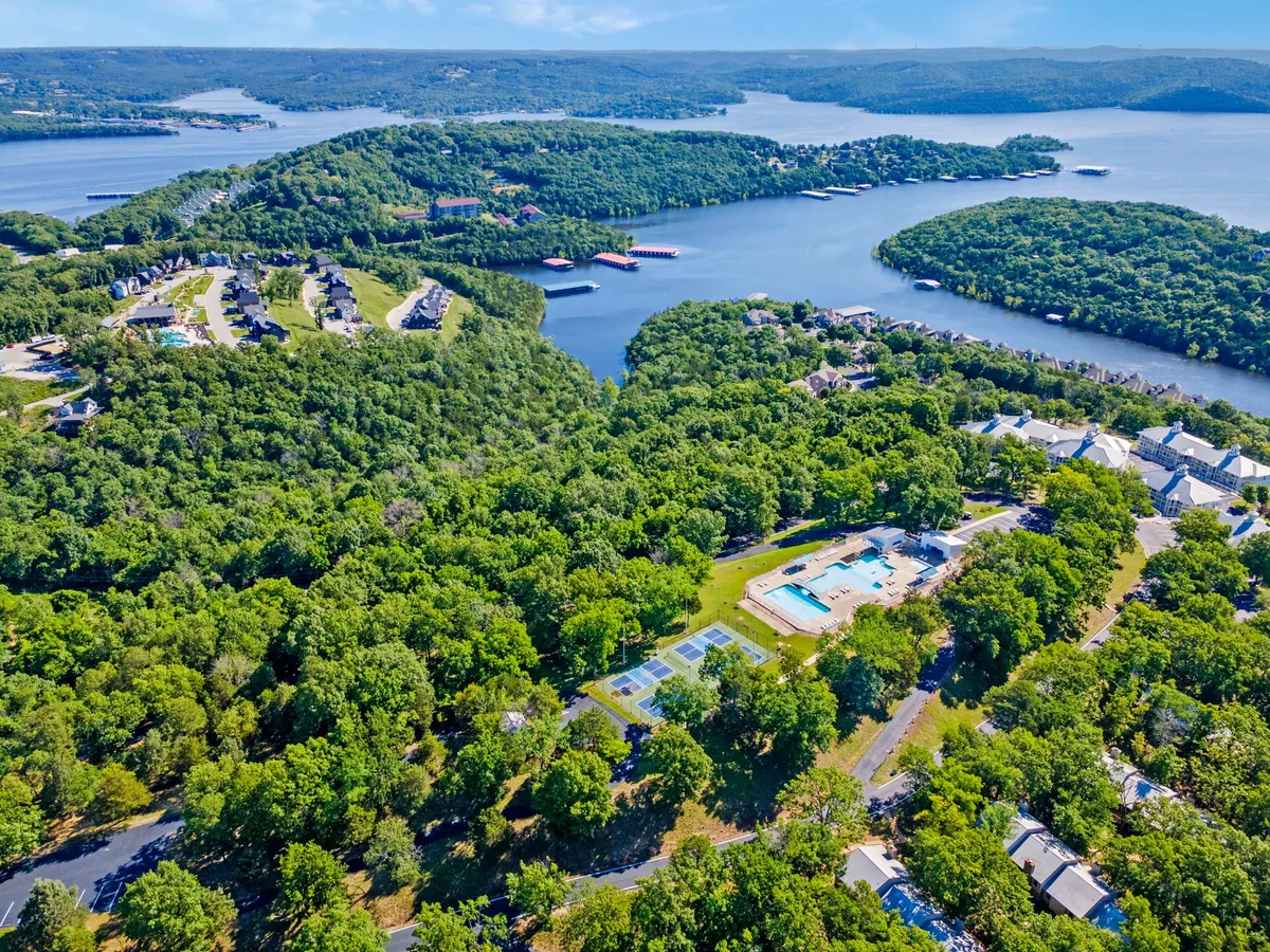 A vibrant exterior shot showcasing lush greenery, a sparkling swimming pool, tennis courts, and expansive waterfront views. The scene captures recreational amenities and a beautiful outdoor setting ideal for group activities and relaxation.