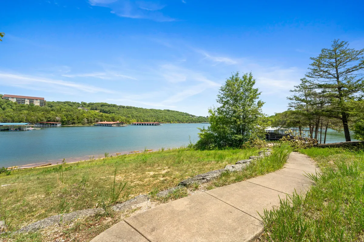 A tranquil lake view with a winding pathway lined by trees and rolling hills in the background. The scene invites leisurely strolls, quiet conversation, and appreciating nature together.