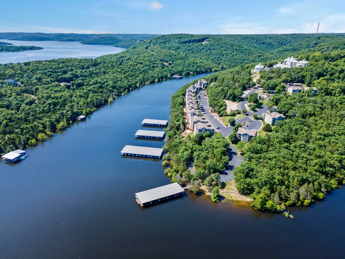 A serene lakefront scene featuring the river, marinas, and residential buildings surrounded by lush greenery. The calm water invites guests to enjoy boating, fishing, or simply relaxing by the shore, with the tranquil mood hinting at picturesque mornings or evenings.