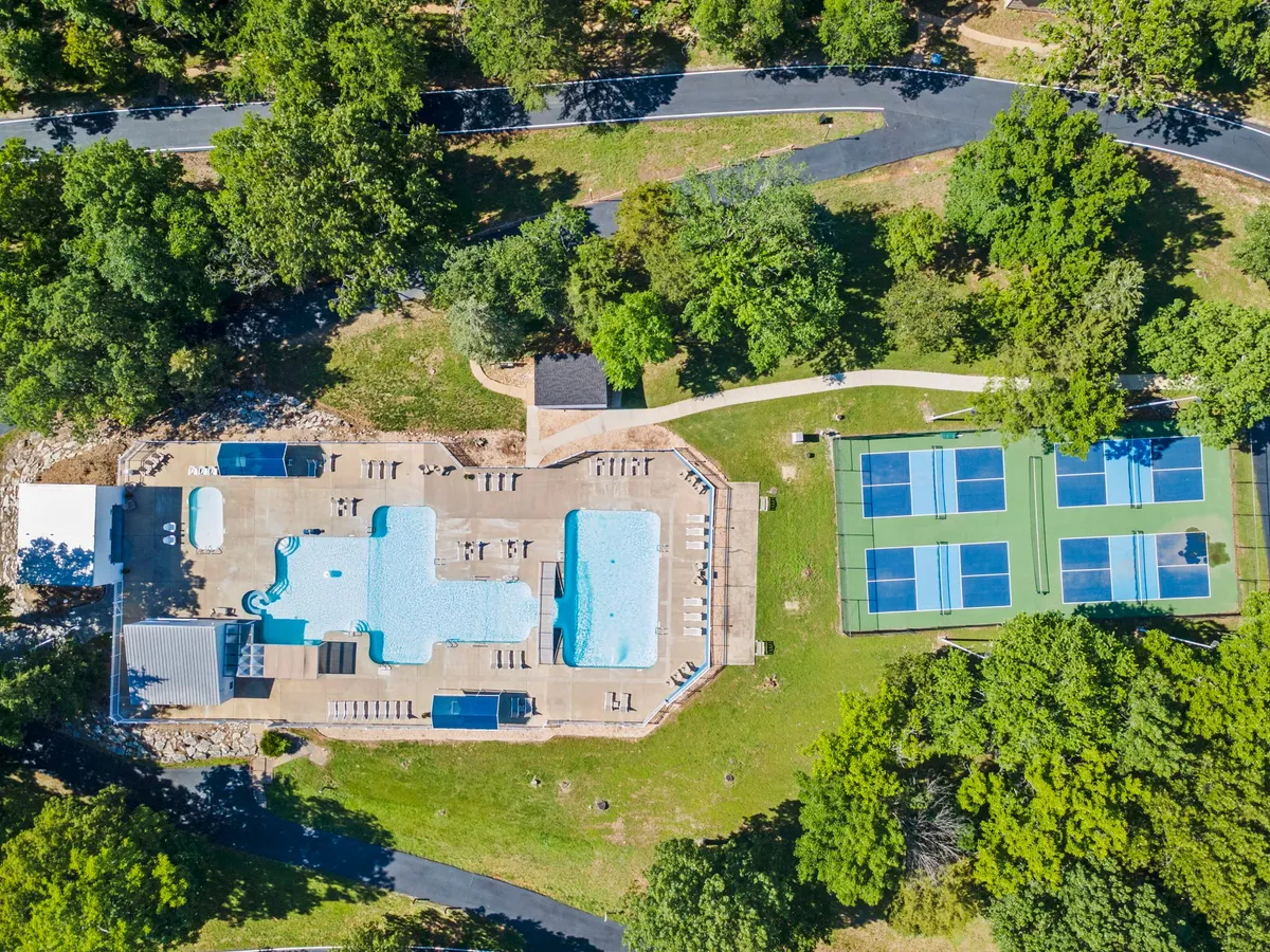 This exterior scene captures a vibrant swimming pool and tennis courts set against a backdrop of trees and open green space. The area is lively yet leisurely, showing guests enjoying both aquatic and court activities, reinforcing the mention of resort amenities like pools and pickleball/basketball in the section.