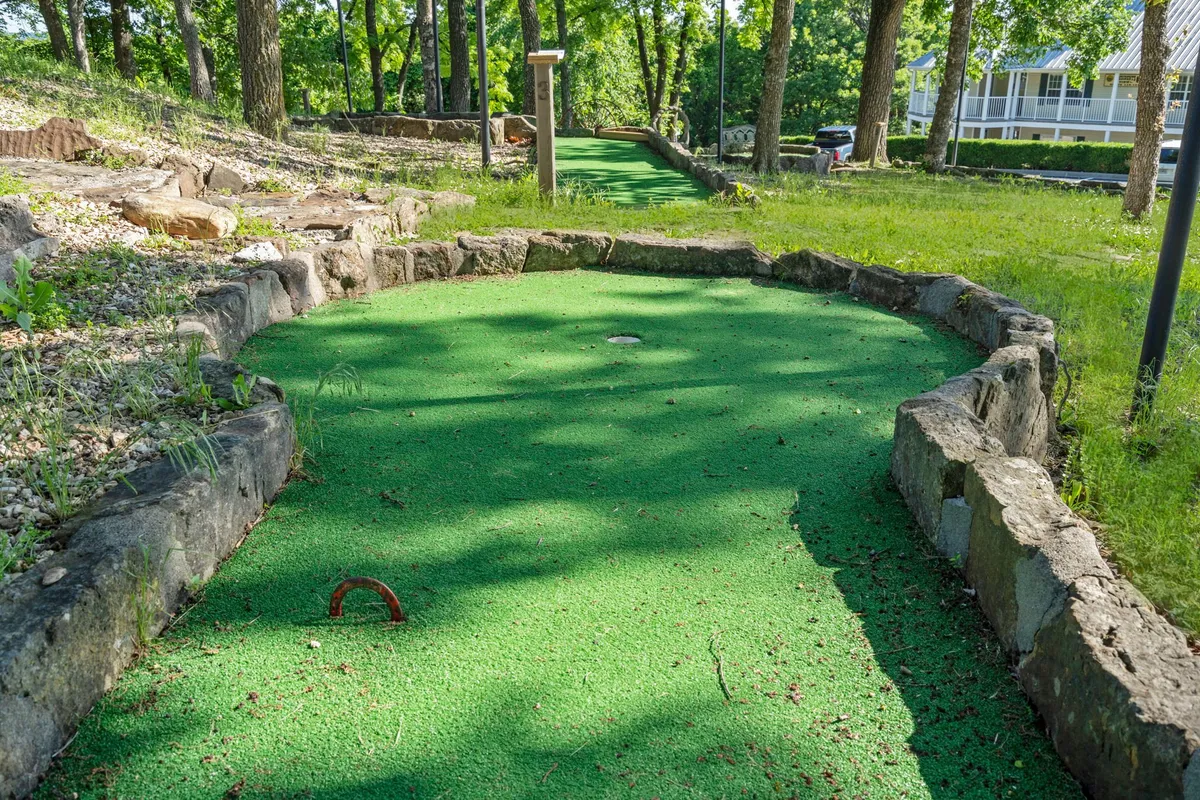 This image features a lush, green mini golf course surrounded by stone borders and mature trees, exuding a lighthearted and fun atmosphere perfect for families and groups. The well-kept landscaping and inviting setting highlight the free, on-site activities available to guests, such as mini-golf, which are mentioned in the section.