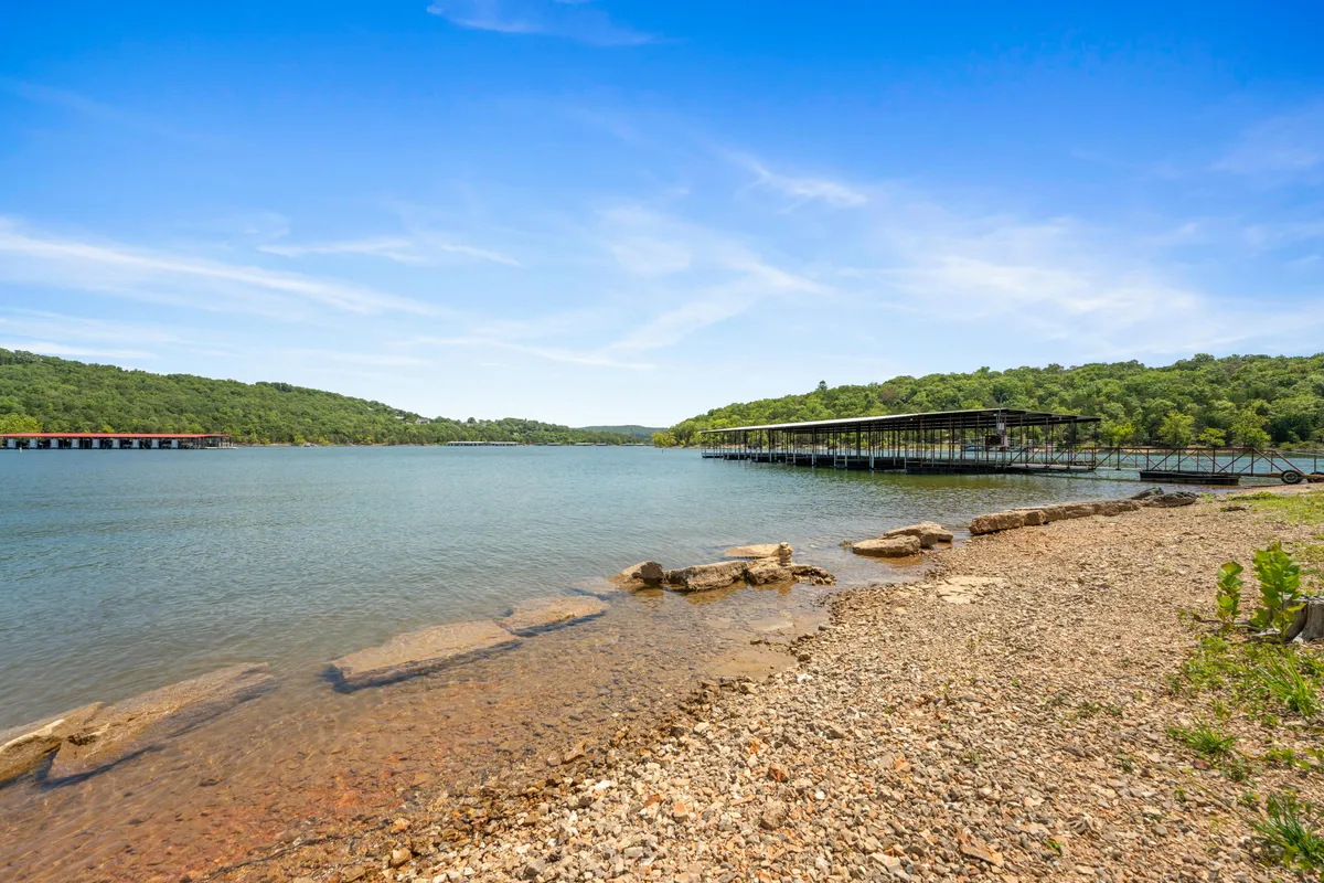 A panoramic view of Table Rock Lake, with docks, a natural shoreline, and rolling green hills in the distance. The setting sun bathes the scene in warm light, evoking peaceful evenings and the beauty of the Ozarks just beyond the balcony.